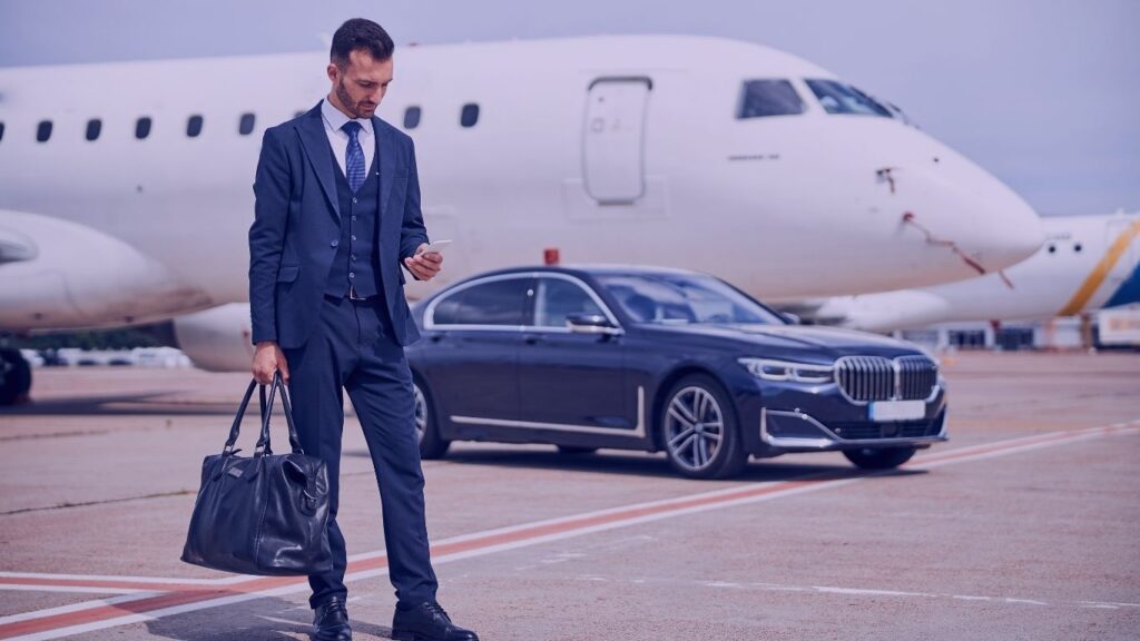 247 IAD chauffeur-stylish-man-business-suit-looking-his-phone-while-standing-front-car-near-plane-Washington-Dulles-International-Airports-Premium-Transportation-Service-Your-247-IAD-chauffeur.