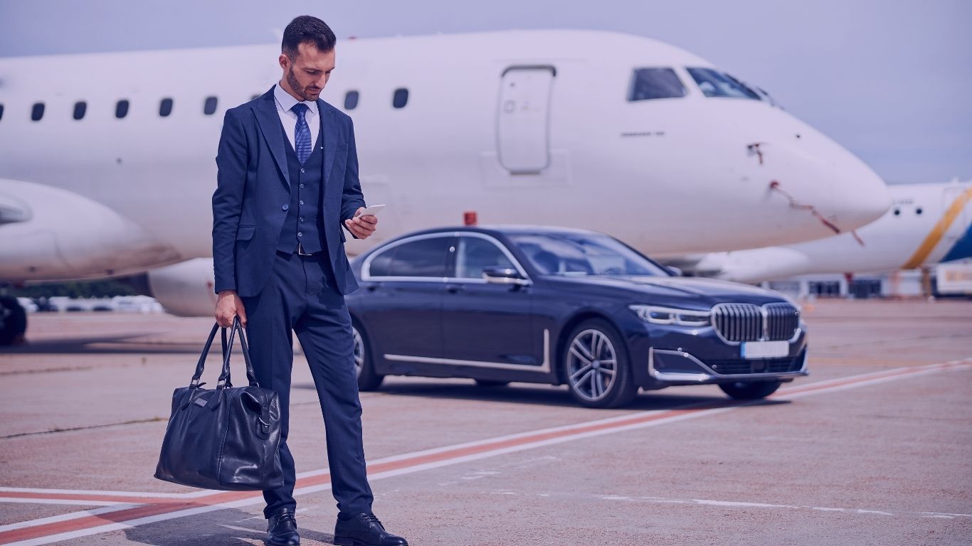 247 IAD chauffeur-stylish-man-business-suit-looking-his-phone-while-standing-front-car-near-plane-Washington-Dulles-International-Airports-Premium-Transportation-Service-Your-247-IAD-chauffeur.